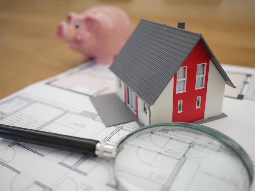 A magnifying glass and a cardboard house miniature on top of a floor plan for mortgage planning