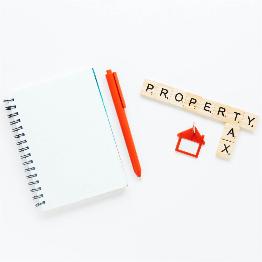 An empty notebook with an orange pen, orange house keychain and wooden blocks spelling out ‘property tax’