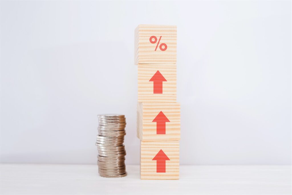 Image of 4 wooden blocks stacked alongside a stack of coins symbolising increase in interest rate percentage and its effects on home loans in Singapore