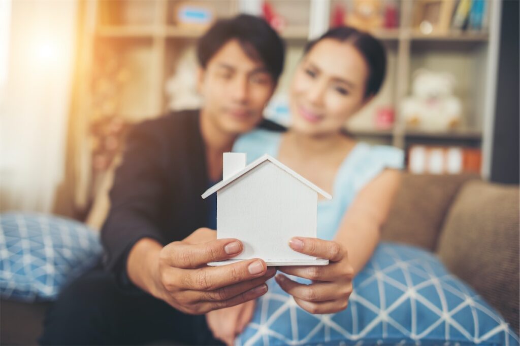 Married couple looking at a cardboard cut-out of their home and discussing how to navigate the rising interest rates in Singapore