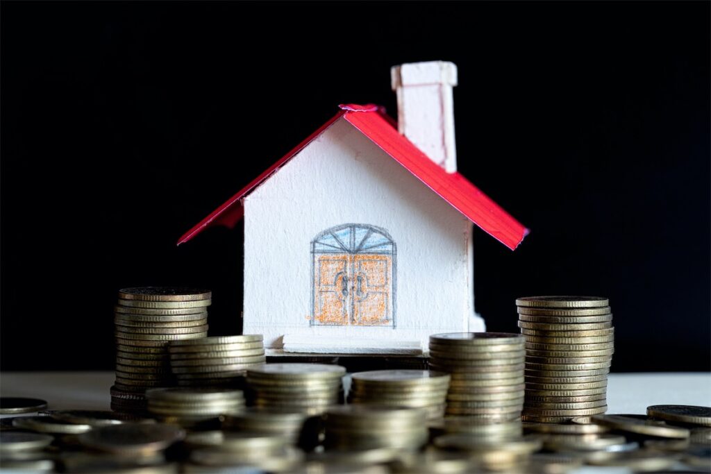 Image of stacks of coins and a private property home made of cardboard to illustrate wealth tax in Singapore